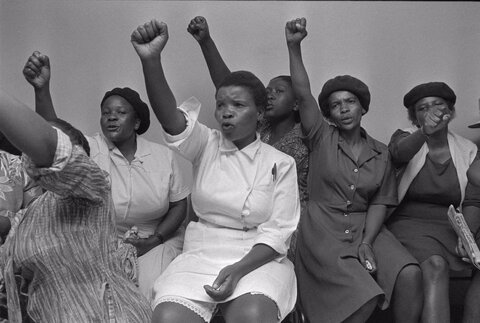 کارگران کمکی بیمارستان باراگوانات در شهرک سووتو ژوهانسبورگ در جریان یک جلسه اتحادیه در آفریقای جنوبی، ۱۶ نوامبر ۱۹۸۵، مشت‌های خود را به هوا پرتاب می‌کنند.