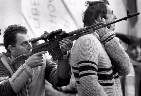 یک غیرنظامی در جریان نبردی بین ارتش، با حمایت غیرنظامیان مسلح، و هواداران چائوشسکو در بلوار ویکتوریا در بخارست، رومانی، ۲۳ دسامبر ۱۹۸۹، تفنگ خود را نشانه گرفته است.