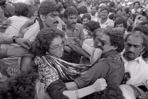 یکی از هواداران، بی‌نظیر بوتو، رهبر اپوزیسیون پاکستان، را پس از آنکه او در واکنش به مردی، موی او را کشید و به او سیلی زد، مهار می‌کند، ۱۰ آوریل ۱۹۸۶.