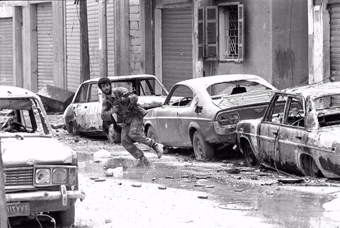 یک شبه‌نظامی شیعه زیر آتش تک‌تیراندازها از کنار خودروهای منهدم‌شده در خیابان اصلی اردوگاه پناهندگان فلسطینی شتیلا در بیروت، جایی که سه روز درگیری بین امل و چریک‌های فلسطینی در جریان بود، می‌دود.